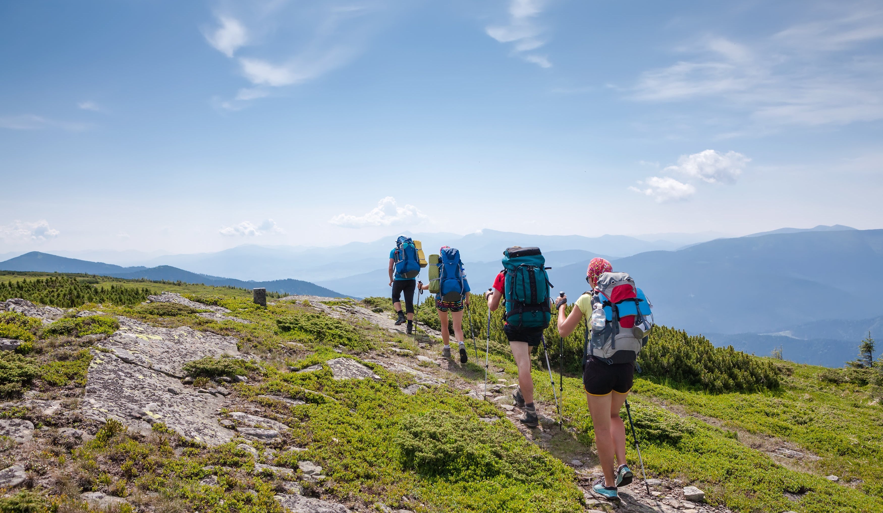 Group of hikers with backpacks on a mountain trail under a blue sky.